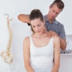 A Male Chiropractic Doctor Stands To Adjust A Sitting Female Patient.