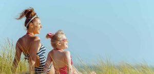 smiling young mother and daughter in swimwear on the seashore looking aside. quiet vacation heaven. protect your hair from sun, heat, and humidity before heading to the beach. blond hair child.