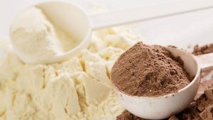 piles of chocolate and vanilla protein powders each with a white plastic scoop sitting on top